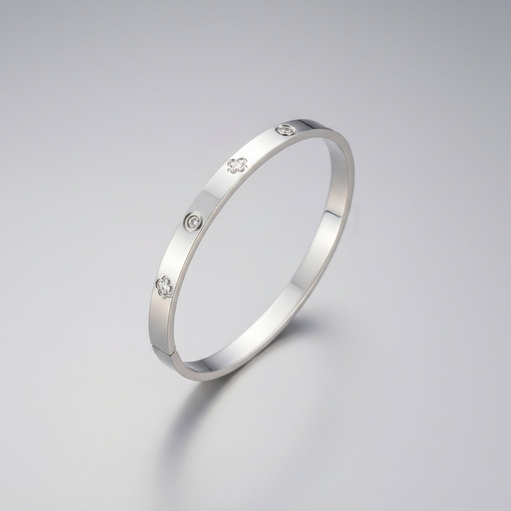 A polished silver bangle bracelet with small clear stones set along the band, displayed on a beige jewelry box.